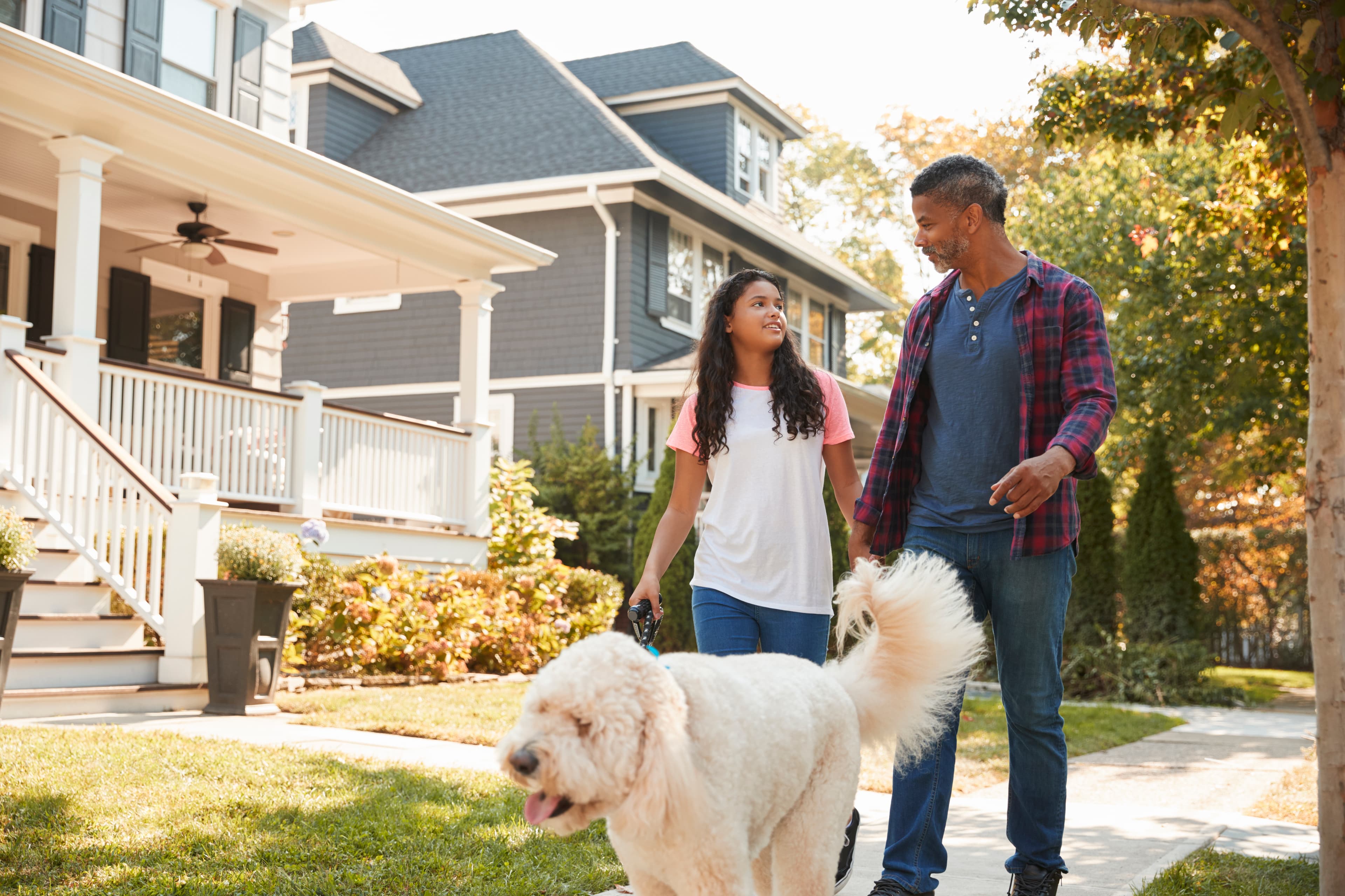 Father and daughter walking dog along suburban street