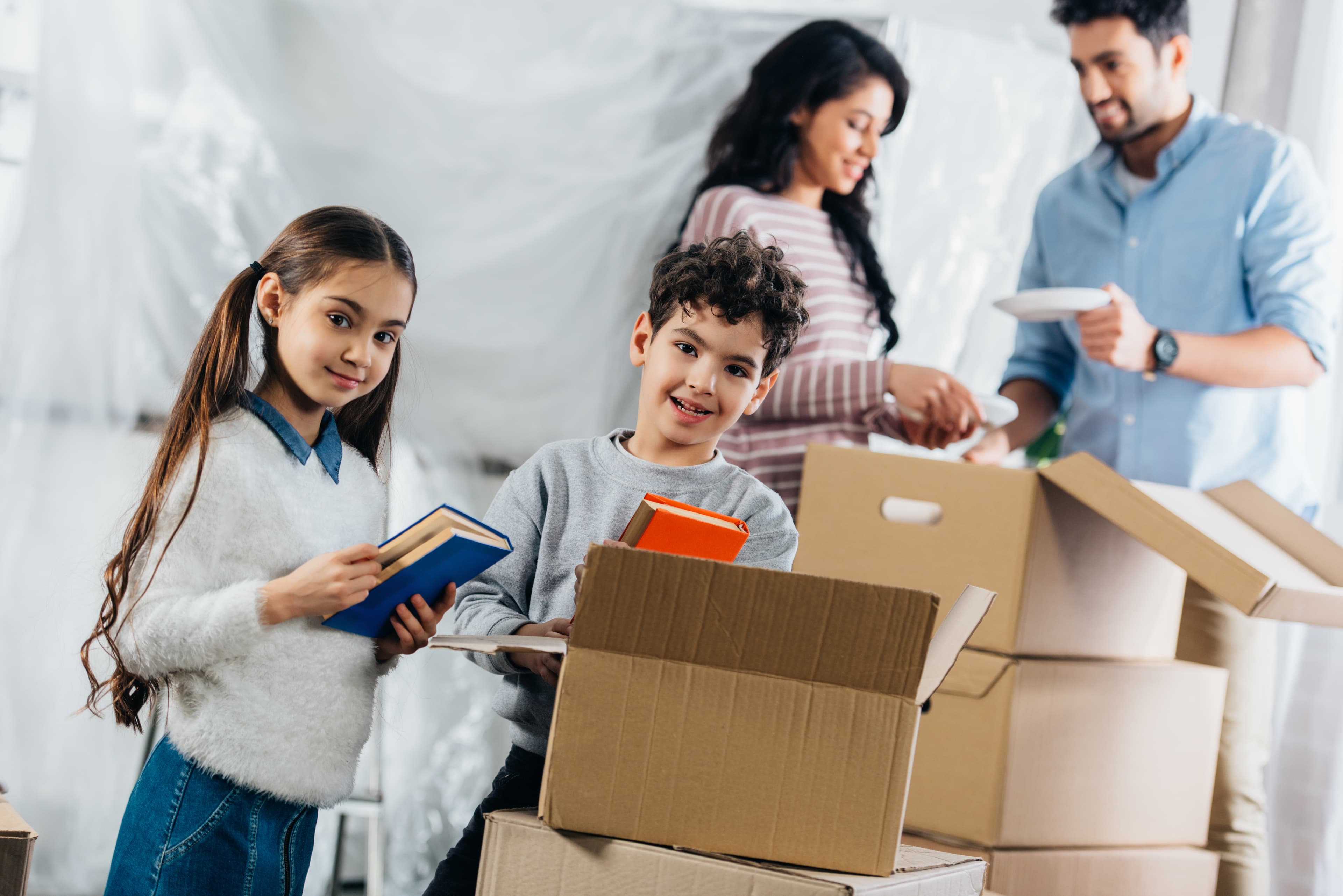 Children holding books while parents unpack